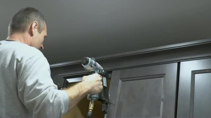建筑工人使用布拉德钉子气枪在白色厨房壁柜框架装饰上进行皇冠造型，配有所有电动工具