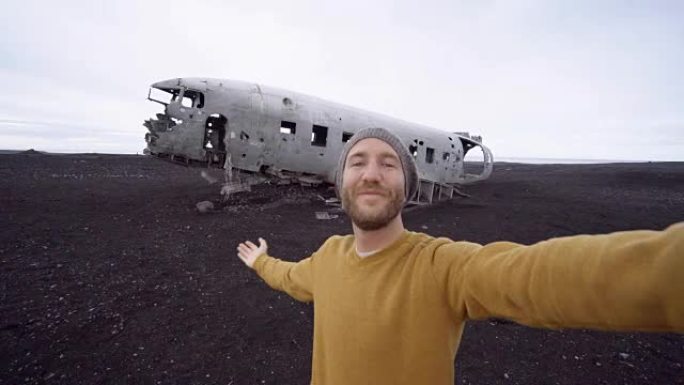 4k-年轻人站在黑沙海滩上的飞机残骸旁拍照，这是冰岛著名的景点，并与残骸合影