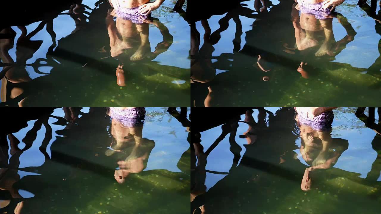 洗浴用来自圣源的冰水。特写镜头，穿着泳裤的人被水反射，他正准备游泳。池底有许多不同的硬币