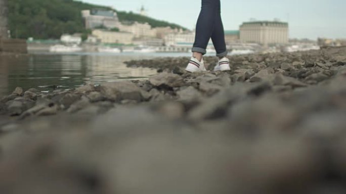 穿着运动鞋的苗条女士的脚在河边的岩石上行走
