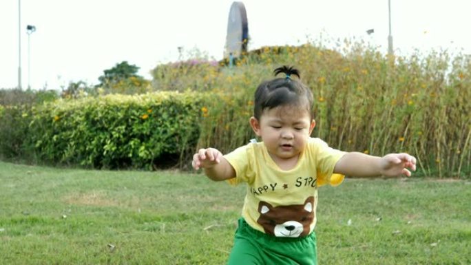 亚洲男婴在公园绿草如茵的草地上散步