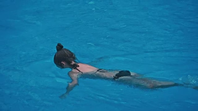 性感的年轻女子在游泳池放松。