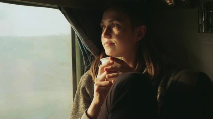 年轻女性在向亚洲火车窗外看时喝水