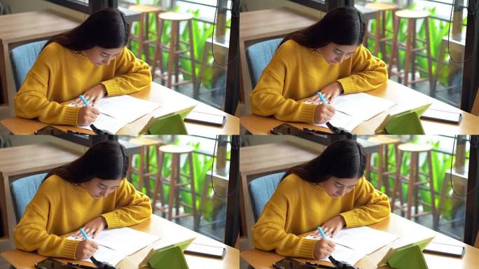 亚洲妇女在咖啡馆的桌子上写文件纸，旅行度假计划，使用笔记本电脑和相机。