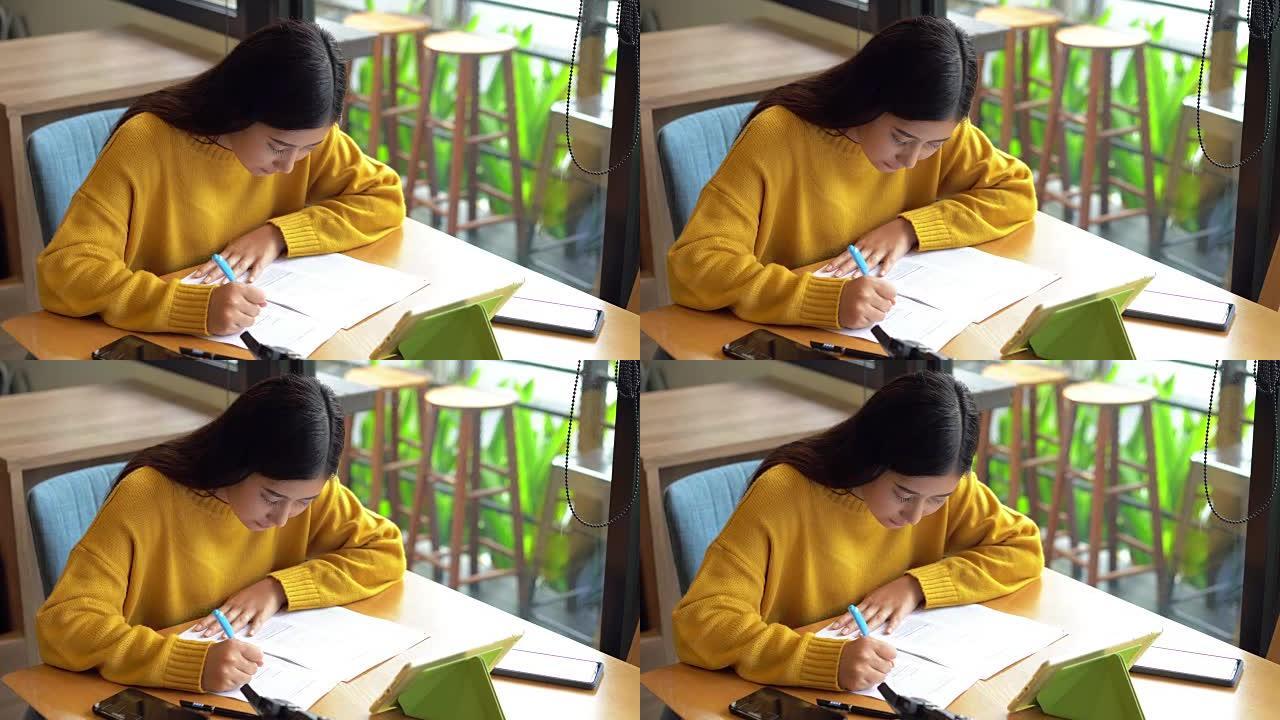 亚洲妇女在咖啡馆的桌子上写文件纸，旅行度假计划，使用笔记本电脑和相机。