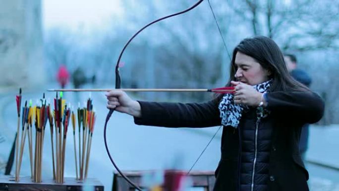 女子弓箭手用4k弓射击。练习射箭的旅游女子对着镜头微笑。女人专注于用箭击中目标。