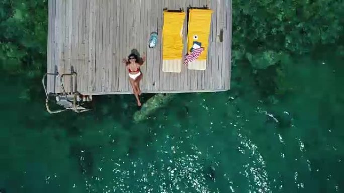 美女独自在木制码头上晒日光浴在海上鸟瞰图4k视频。
