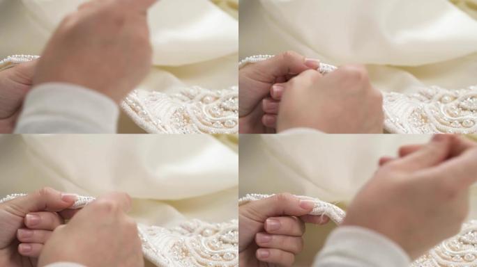双手在婚纱下摆缝制串珠花边的特写镜头