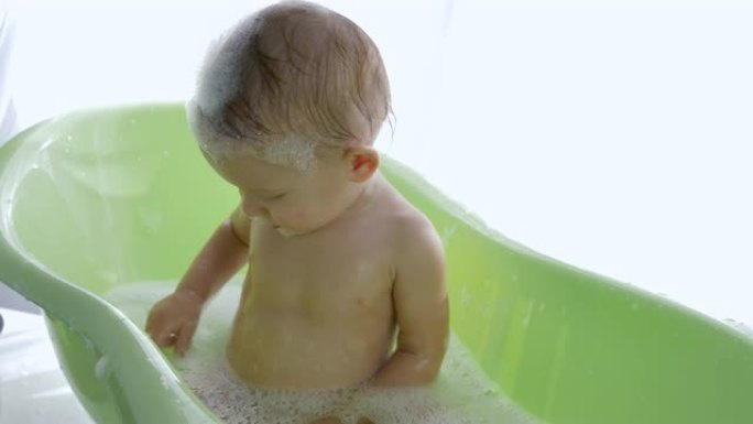 给婴儿洗澡，小孩变成泡沫，坐在明亮的房间的浴缸里
