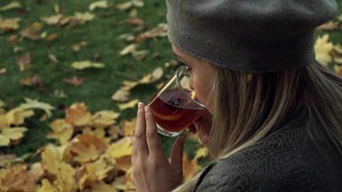 年轻女孩在秋季公园喝热酒