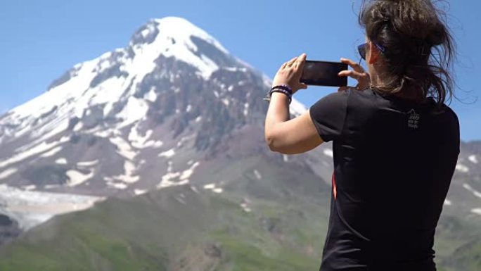 一名年轻女子正在用智能手机在山上拍下美丽的风景。