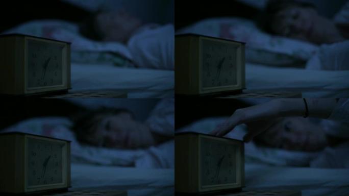 一个穿着睡衣的女孩躺在床上，看着闹钟无法入睡的特写镜头。从几个小时到面对女孩的可变焦点。美国之夜的影