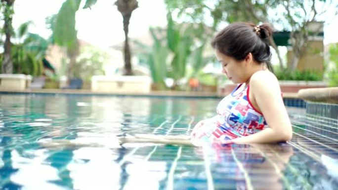 快乐的孕妇在游泳池里放松时，用爱抚摸她的肚子。