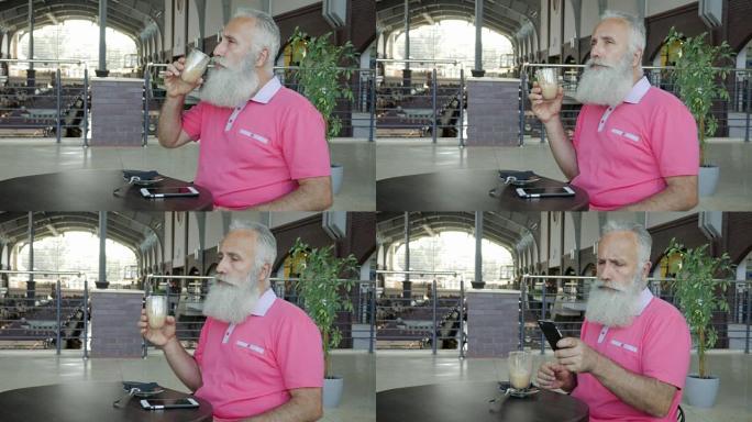 大胡子男子喝卡布奇诺咖啡，并在咖啡馆的智能手机中查看消息