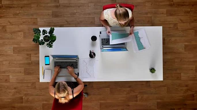 两个同事在笔记本电脑上打字时检查纸质图表，手机上的蓝屏，滚动，在办公室