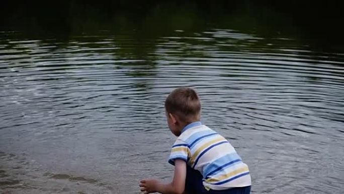 小男孩尖叫着，愤怒地把水桶里的水倒进河里。儿童在大自然中玩耍