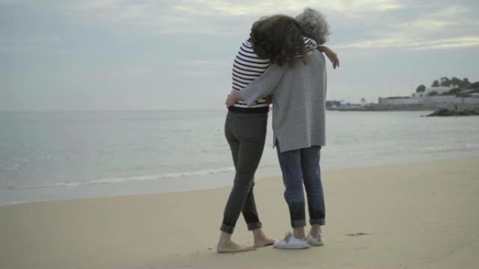 快乐的资深母亲和成年女儿在沙滩上拥抱。