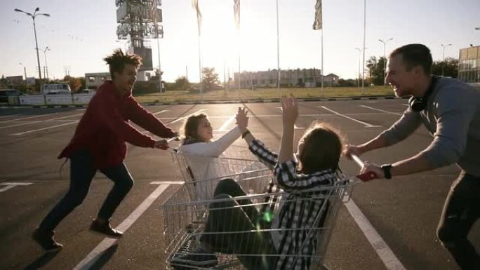 年轻的千禧一代人们用购物车赛车 -- 快乐的疯狂朋友在停车场玩手推车。corts里的女孩互相击掌。青