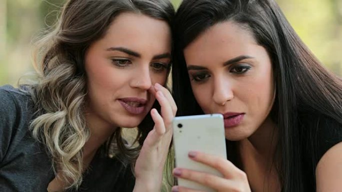地道的朋友一起在户外检查手机。女孩看着并拿着智能手机聊天交换八卦