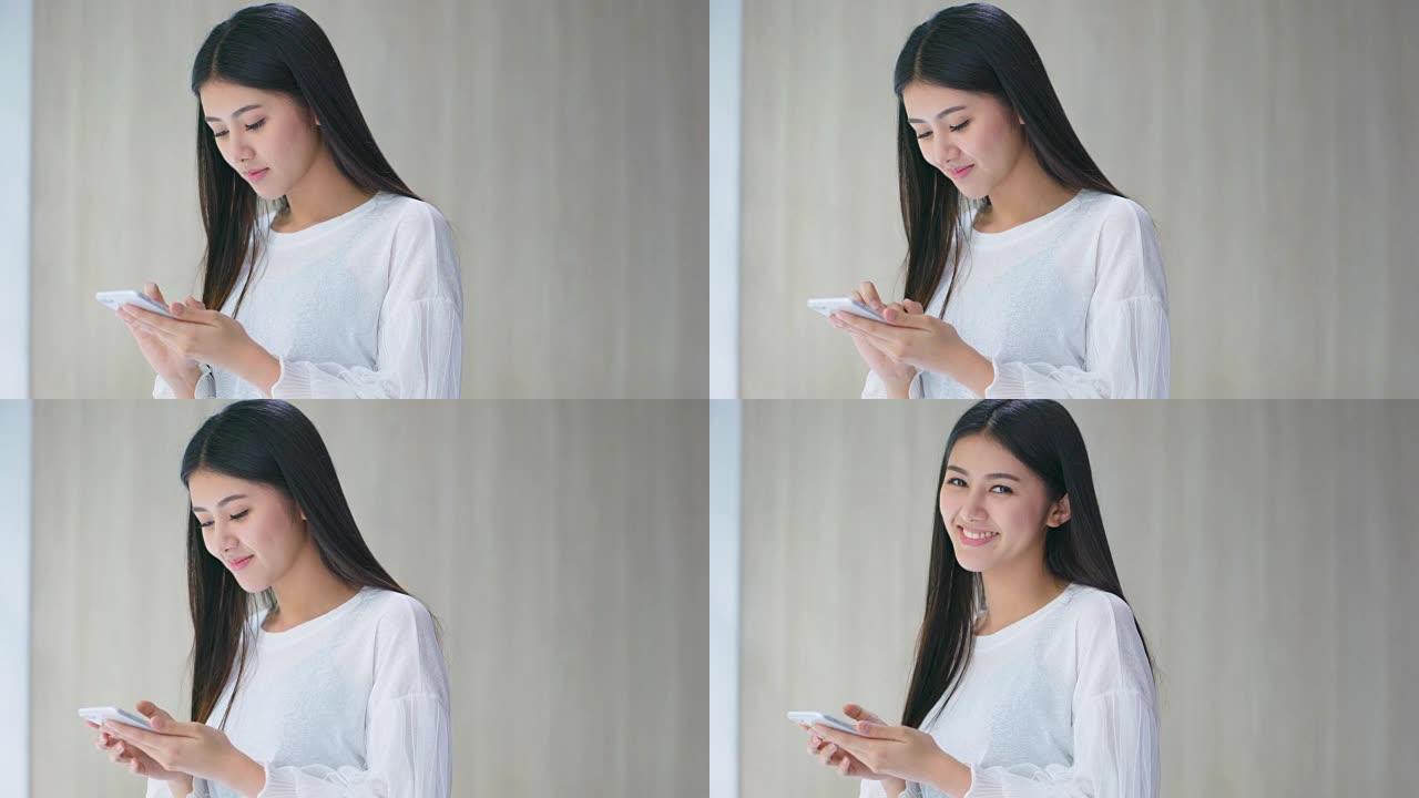 美丽的亚洲女人享受幸福手用智能手机靠近窗户