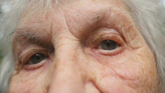老祖母看着相机的肖像。闭上周围有皱纹的老年妇女的眼睛。