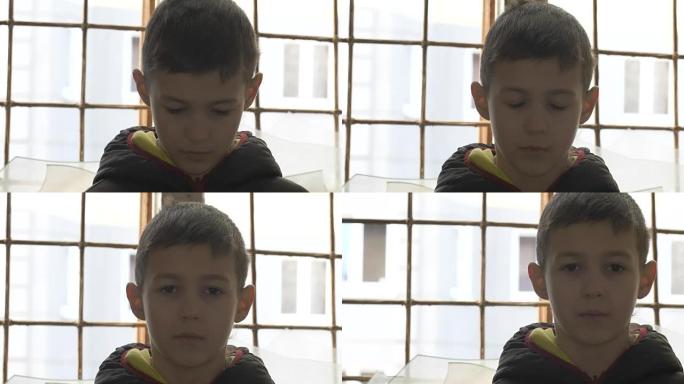 肖像瘦弱的难民男孩独自站在破碎的窗户旁，看着相机