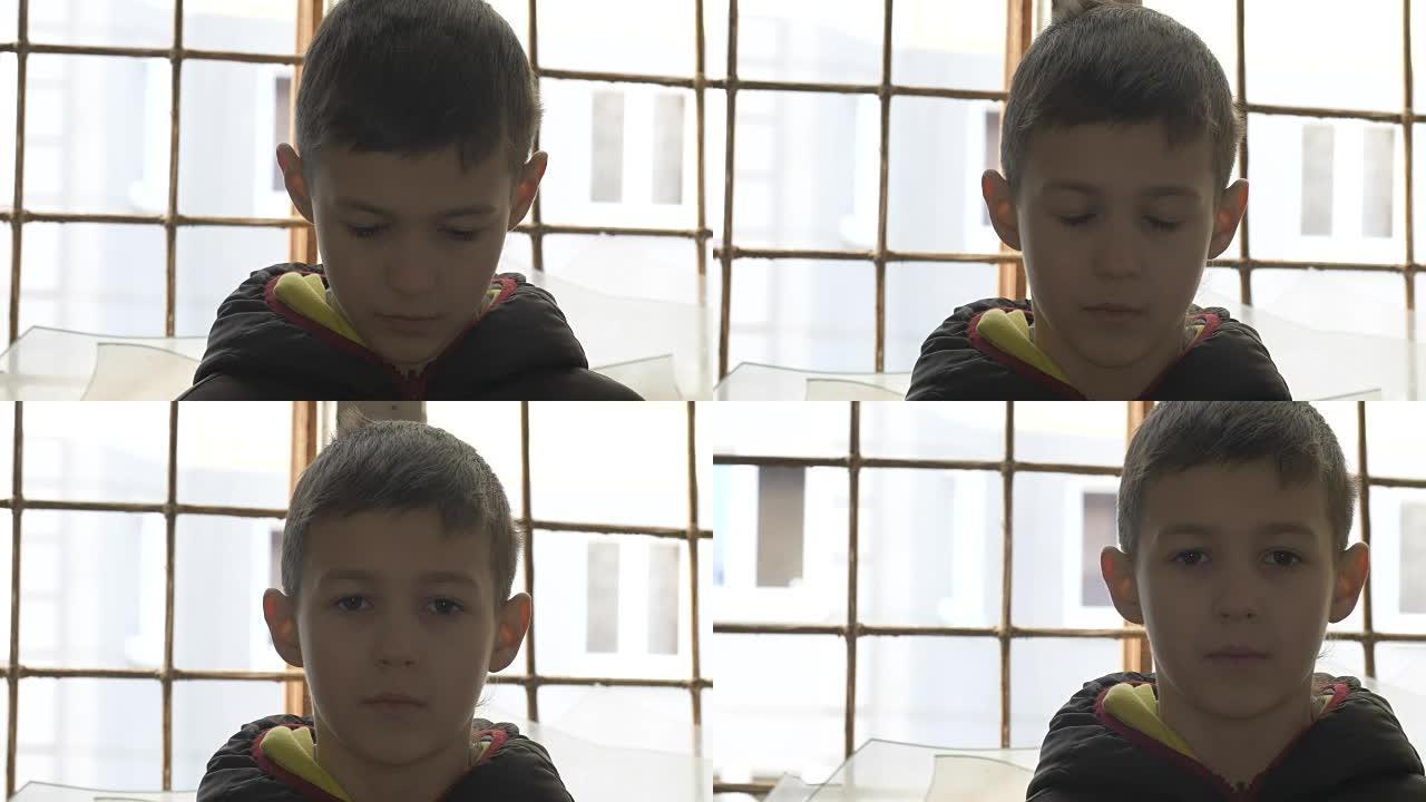 肖像瘦弱的难民男孩独自站在破碎的窗户旁，看着相机