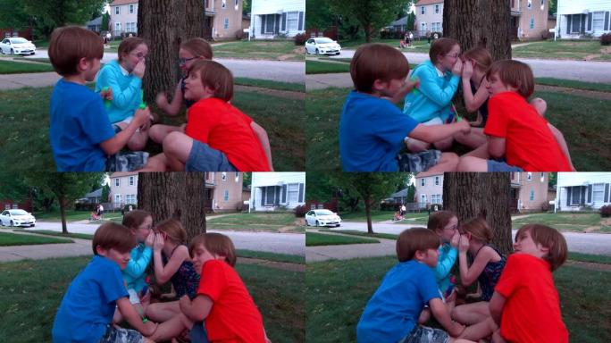 四个孩子坐在前院一棵树边的绿色草地上玩泡泡