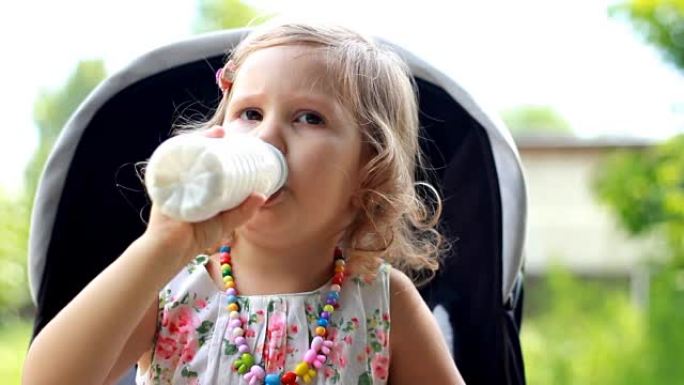 女童坐在婴儿车中，从瓶子或开菲尔中喝牛奶饮料。