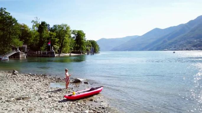 无人驾驶飞机在湖岸拍摄的年轻女子，红色独木舟在地图上寻找方向，准备在夏天在瑞士的山湖探索大自然