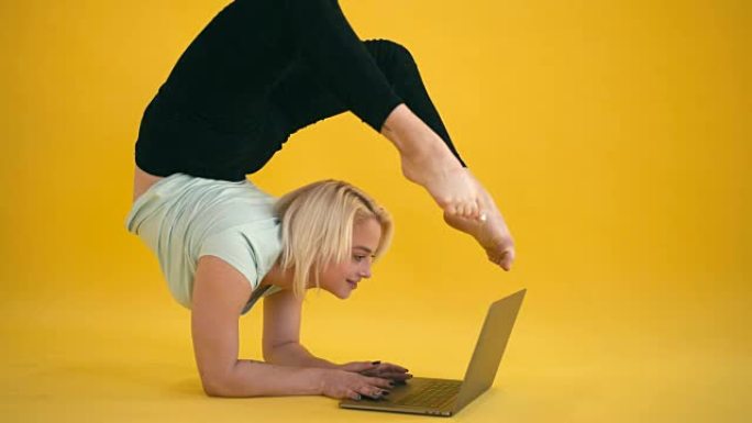 金色模特尺寸加练习瑜伽倒立姿势，并在黄色背景下使用笔记本电脑