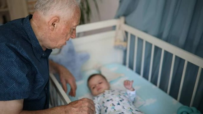 爷爷和躺在婴儿床里的孙子一起玩