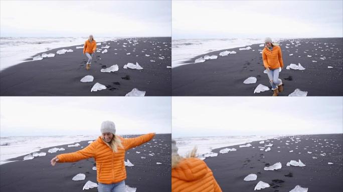 年轻女性游客女性在Jokulsarlon Diamond's beachx的黑沙滩上跳跃和嬉戏