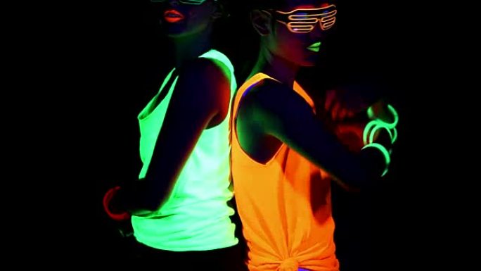 女人用紫外线的面漆，发光的手镯，发光的眼镜，衣服在镜头前互相对着对方跳舞，向下倾斜。高加索人和亚洲女