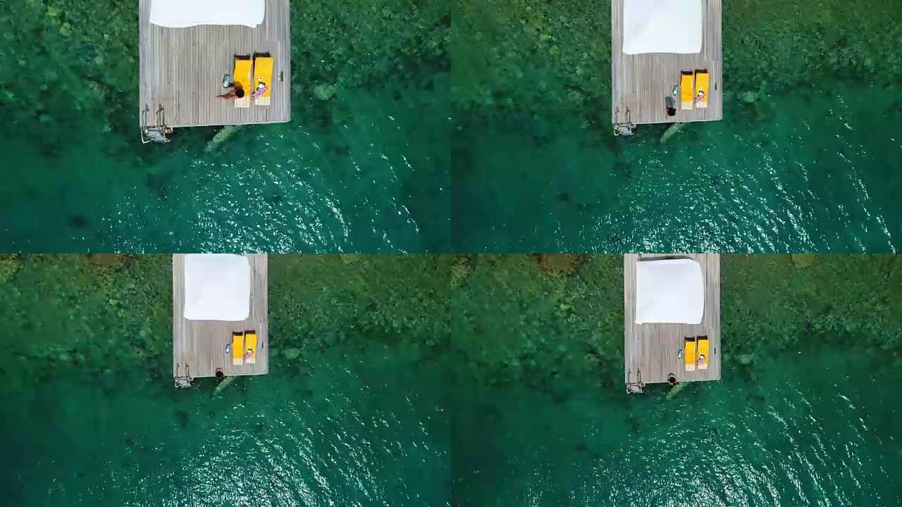 美女独自在木制码头上晒日光浴在海上鸟瞰图4k视频。