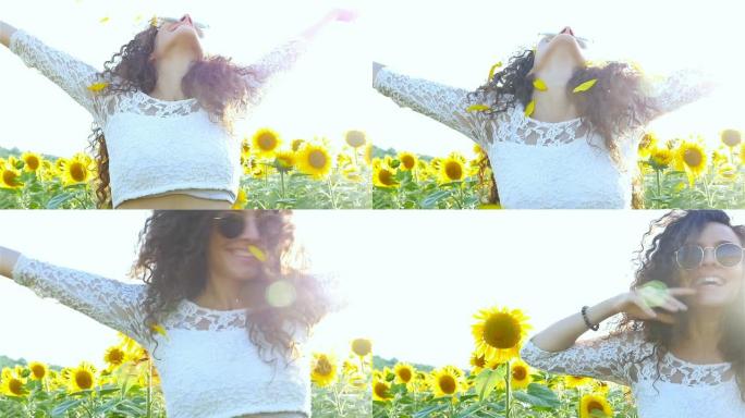 美丽的幸福女孩女人在日落时在向日葵田上头顶上撒播向日葵花瓣。自由概念。慢动作