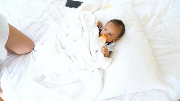 手持俯视图: 母亲躺在白色床上时，给婴儿喝奶瓶中的牛奶和水