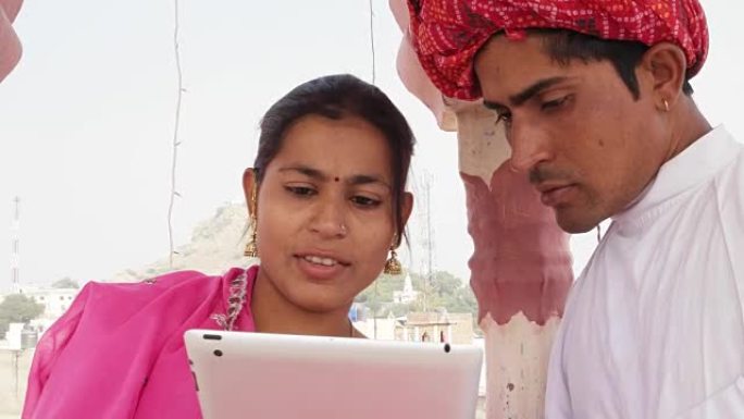 在印度，一对拉贾斯坦夫妇穿着粉色纱丽和红色头巾，在平板电脑上学习和教学