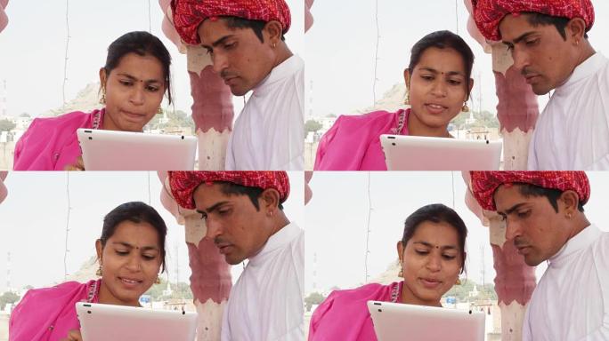 在印度，一对拉贾斯坦夫妇穿着粉色纱丽和红色头巾，在平板电脑上学习和教学