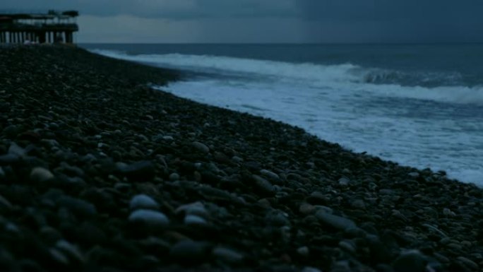 在雨云的背景下，海浪在大海上的暴风雨中拍打着鹅卵石