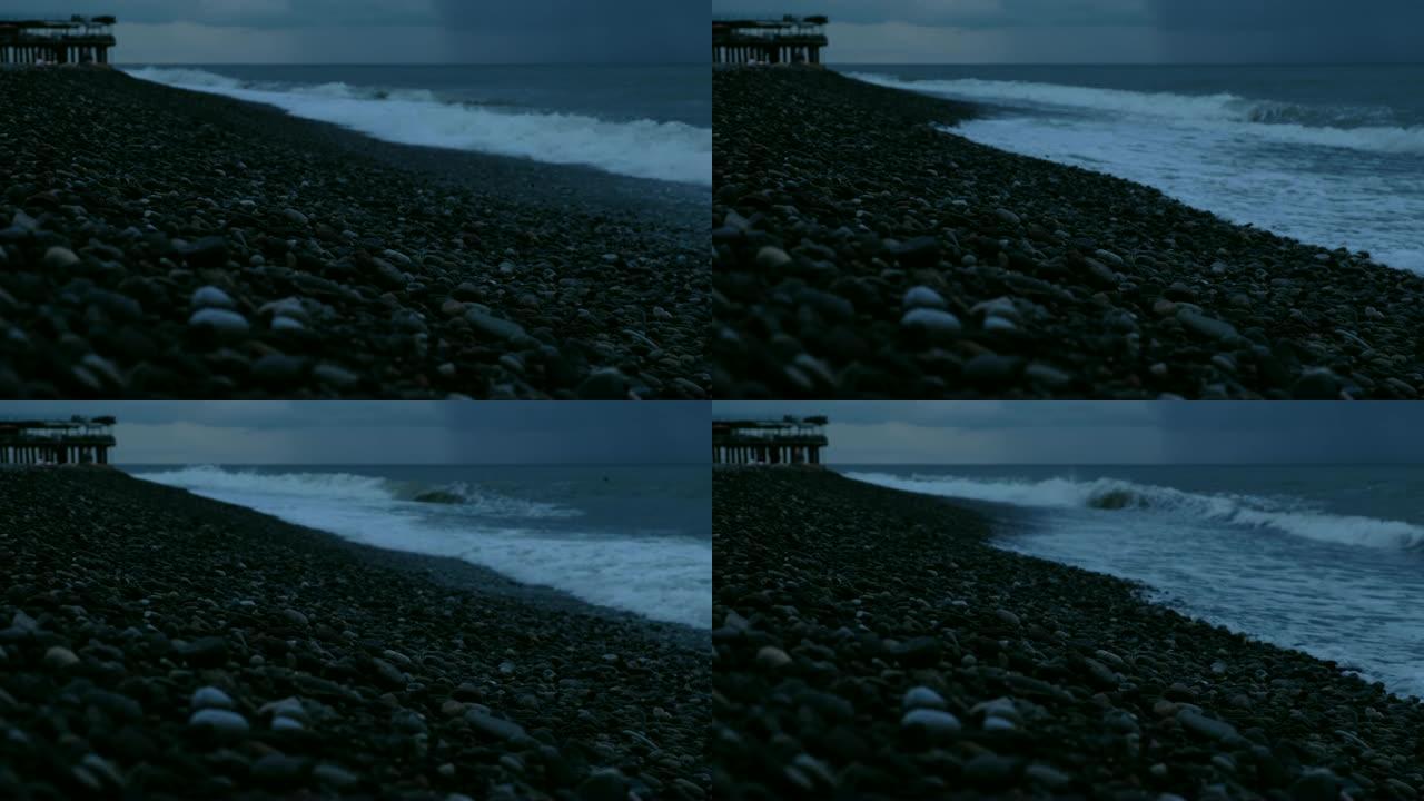 在雨云的背景下，海浪在大海上的暴风雨中拍打着鹅卵石