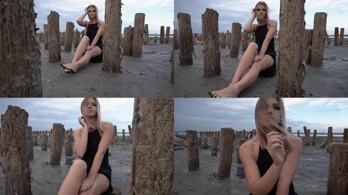 年轻的金发女子坐在盐峡湾海岸，周围是木桩，多云的天气