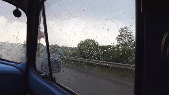 在雨天行驶时，透过旧复古汽车的侧窗观看。在乡下开车时，雨滴落在老式汽车的玻璃上。关闭慢动作