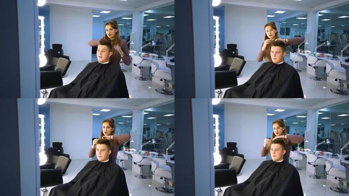 美容院里的一个年轻帅哥。那家伙正坐在扶手椅上。理发师给她理发。那家伙坐在镜子前。他很高兴。