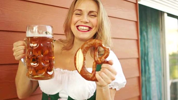 啤酒和椒盐卷饼的女孩，啤酒节的酒吧招待。性感的白齿微笑，红唇，真诚的喜悦。巴伐利亚国家服装