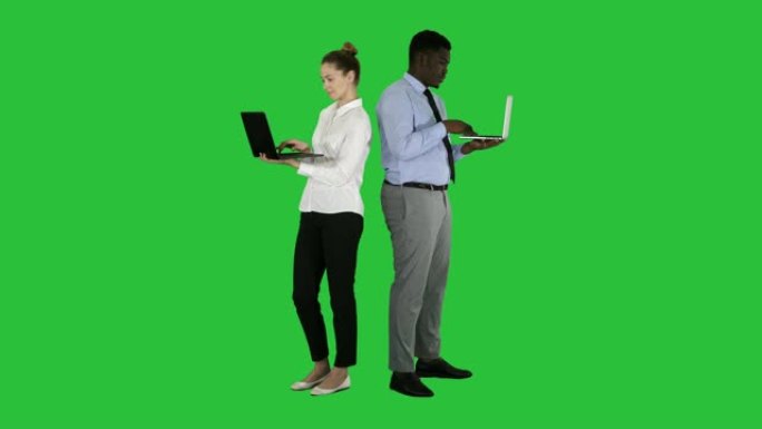 夫妇背靠背站立并在绿色屏幕上的笔记本电脑上工作，色度键