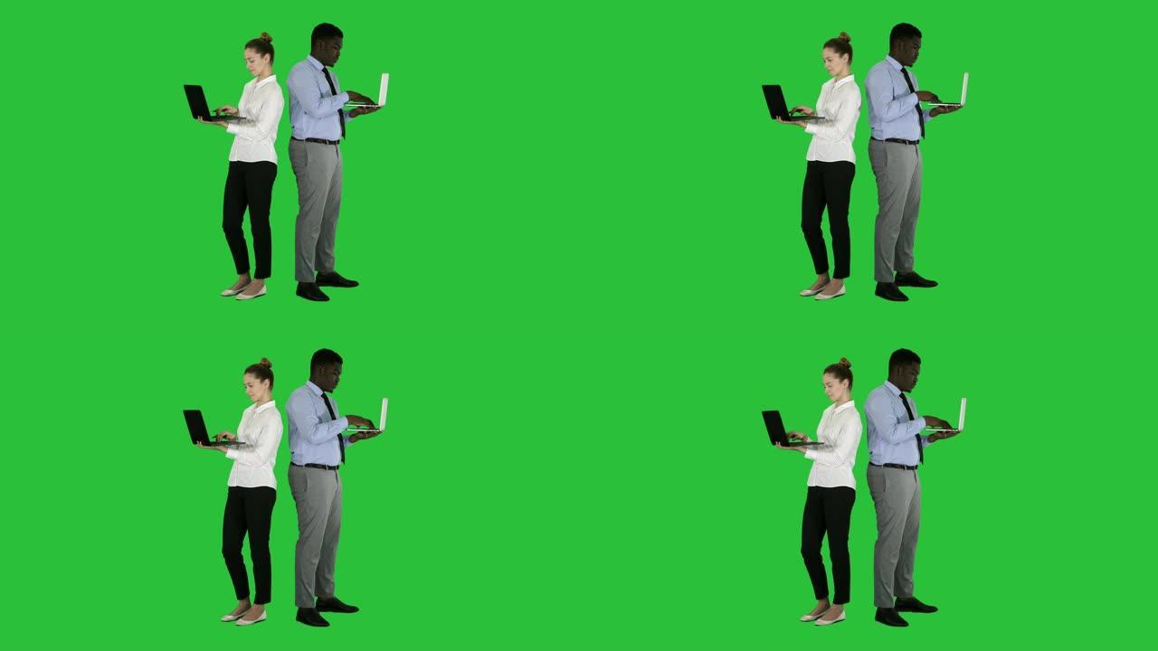 夫妇背靠背站立并在绿色屏幕上的笔记本电脑上工作，色度键