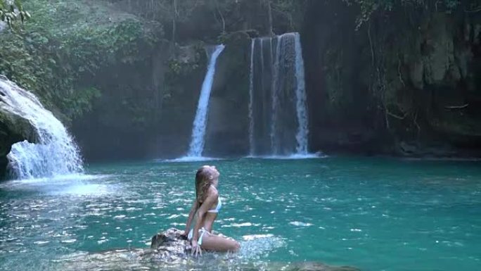 年轻女子在菲律宾宿雾岛上美丽的瀑布上在水中扔头发。人们旅行热爱自然的概念。一个人只在和平的环境中享受