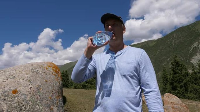 盖帽男子从山上和蓝天背景的瓶子里喝水