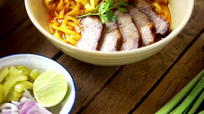 倾斜相机: Khao Soi食谱，泰国北部风味咖喱面汤和猪肉放在木桌上。